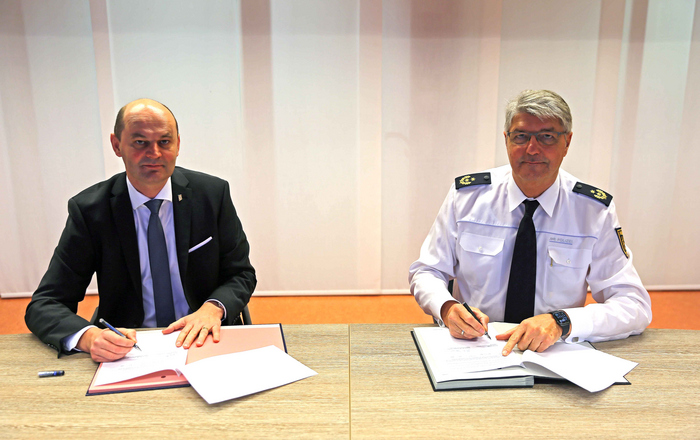 Rektor Prof. Dr. Stephan Trahasch (links) und Polizeipräsident Reinhard Renter (rechts) sitzen bei der Unterzeichnung der Kooperationsvereinbarung an einem Tisch.